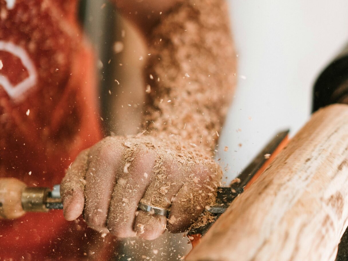 Carpenter shaping wood on a lathe with precision, sawdust flying – showcasing skilled labor in the construction industry, as highlighted by Matt Roberts on A Few Good Lads' blog.